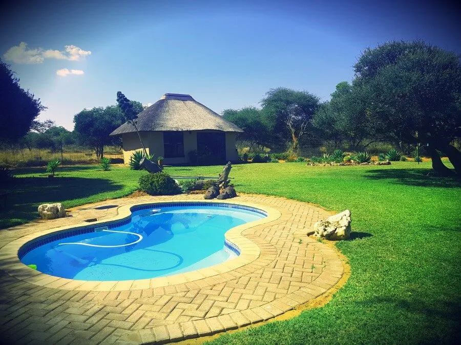 A thatched lodge beside a kidney-shaped pool and green lawn